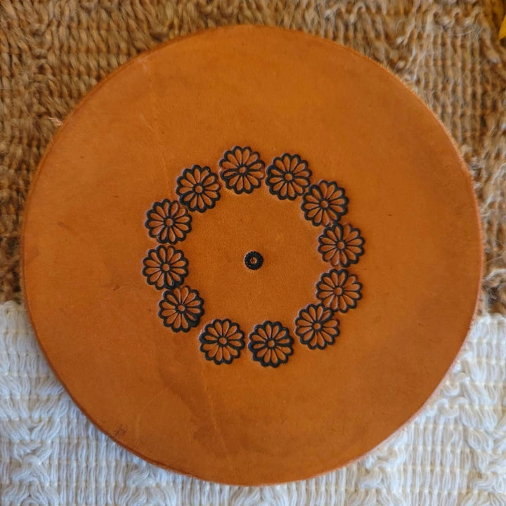 Front view of round leather coaster with floral circle stamped pattern and medium stain finish