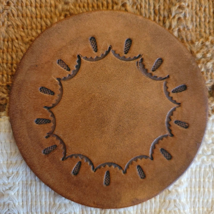 Front view of round leather coaster with a circular scallop and teardrop stamped pattern and medium stain finish