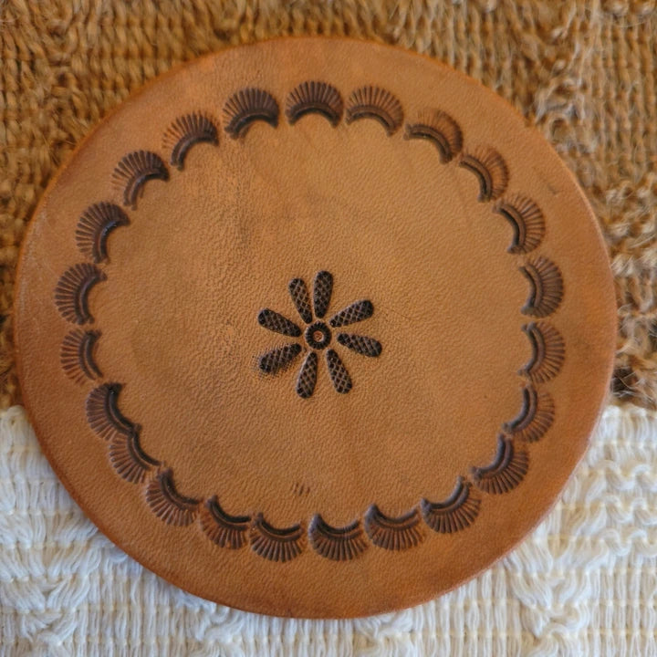 Front view of round leather coaster with scalloped edge stamps in a circular pattern and a center floral design, medium stain finish