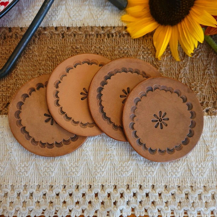 Set of four leather coasters with scalloped edge stamps in a circular pattern and a center floral design, medium stain finish