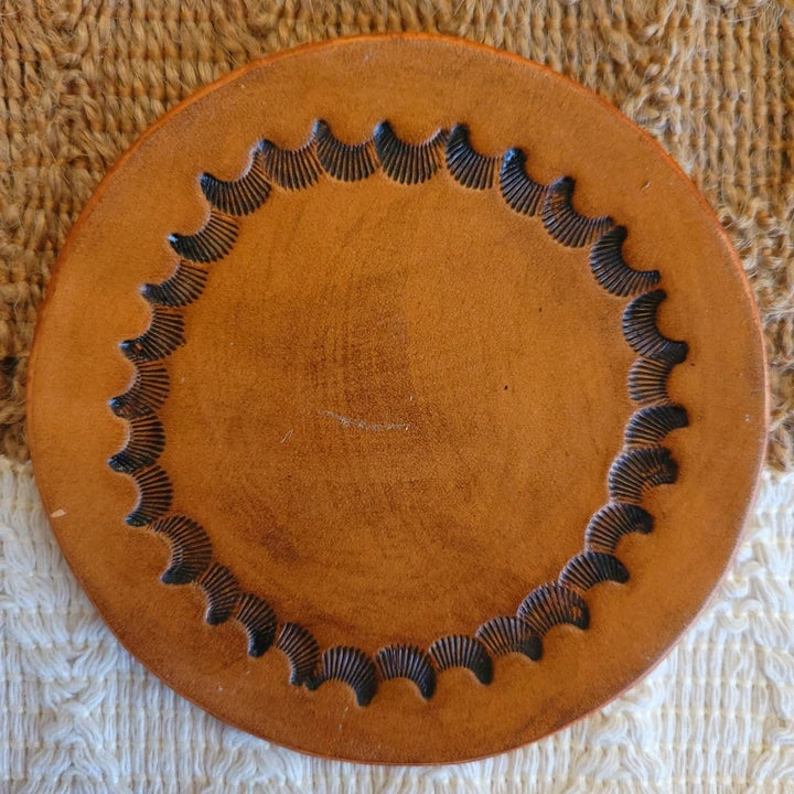 Front view of single-layer leather coaster with inward-facing starburst border design and medium stain finish