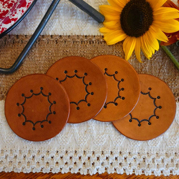 Set of four single‑layer leather coasters in a medium stain with an inward scalloped circular border and dots at each point.