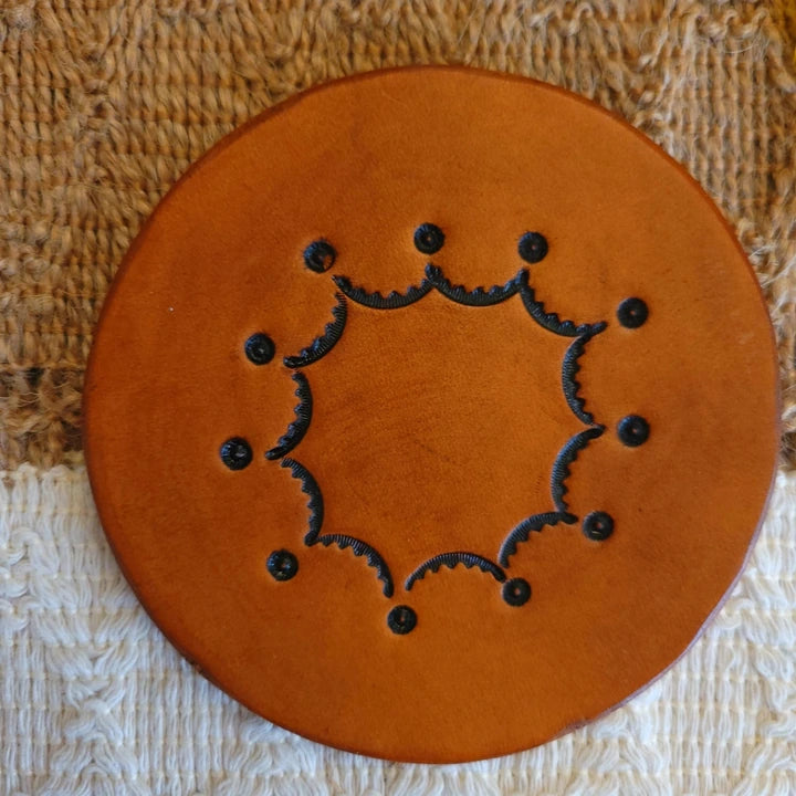 Front view of a single‑layer leather coaster, medium stain, featuring an inward scalloped circular border with dots at the points.