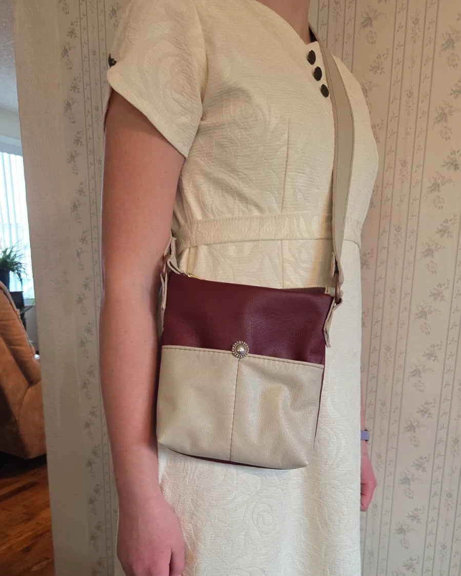 a lady wearing a beige and rust leather crossbody purse with a zipper closure