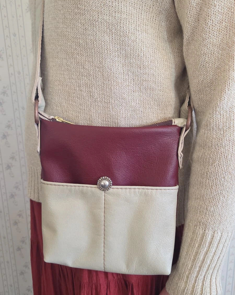 a lady wearing a beige and rust leather crossbody purse with a zipper closure