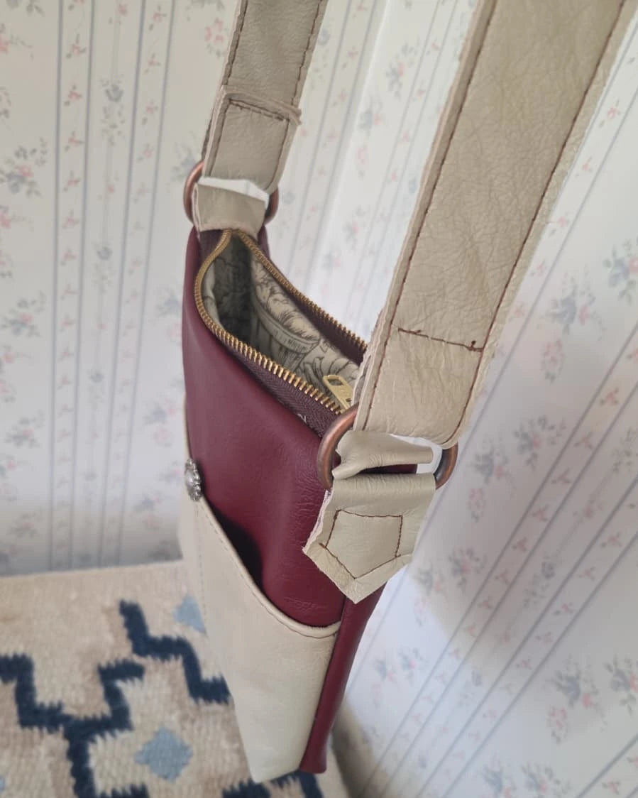 the top view of a beige and rust leather crossbody purse with a zipper closure