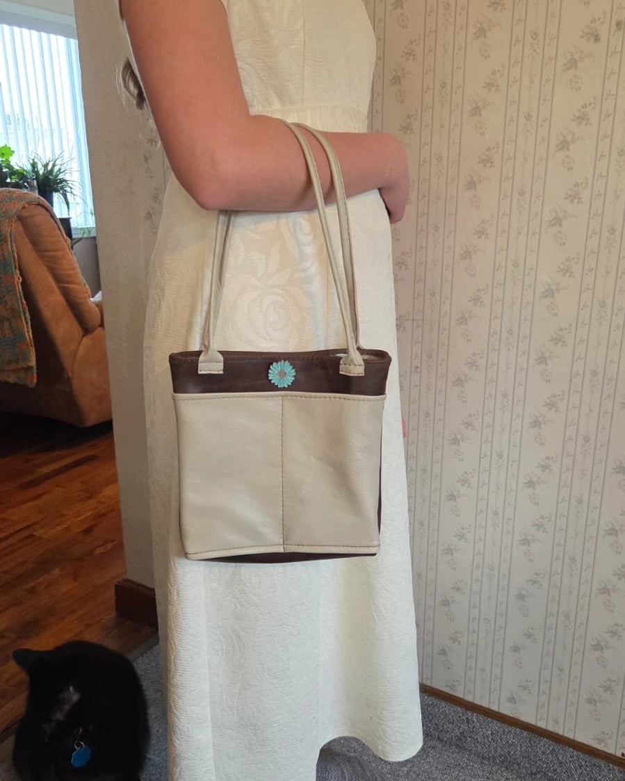 lady holding a beige and brown handbag with a blue flower snap closure